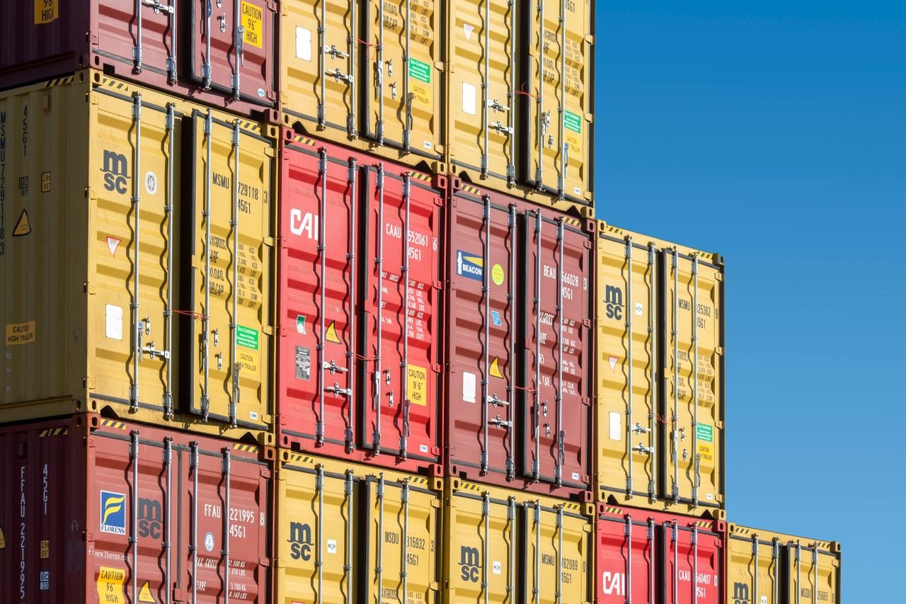 about-us Colorful shipping containers stacked against a clear blue sky, representing global trade and transportation.
